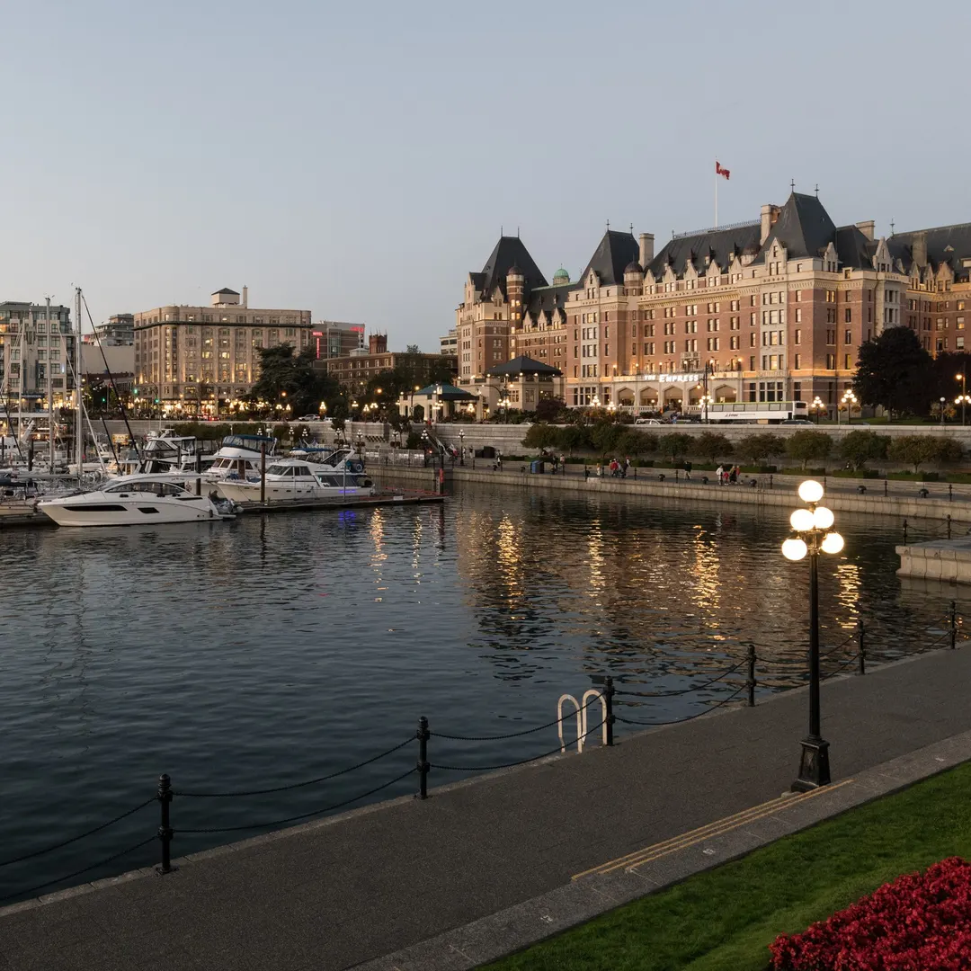 Victoria's Inner Harbour at dusk — causeway lamps lit, boats moored, the Empress Hotel above the sea wall.