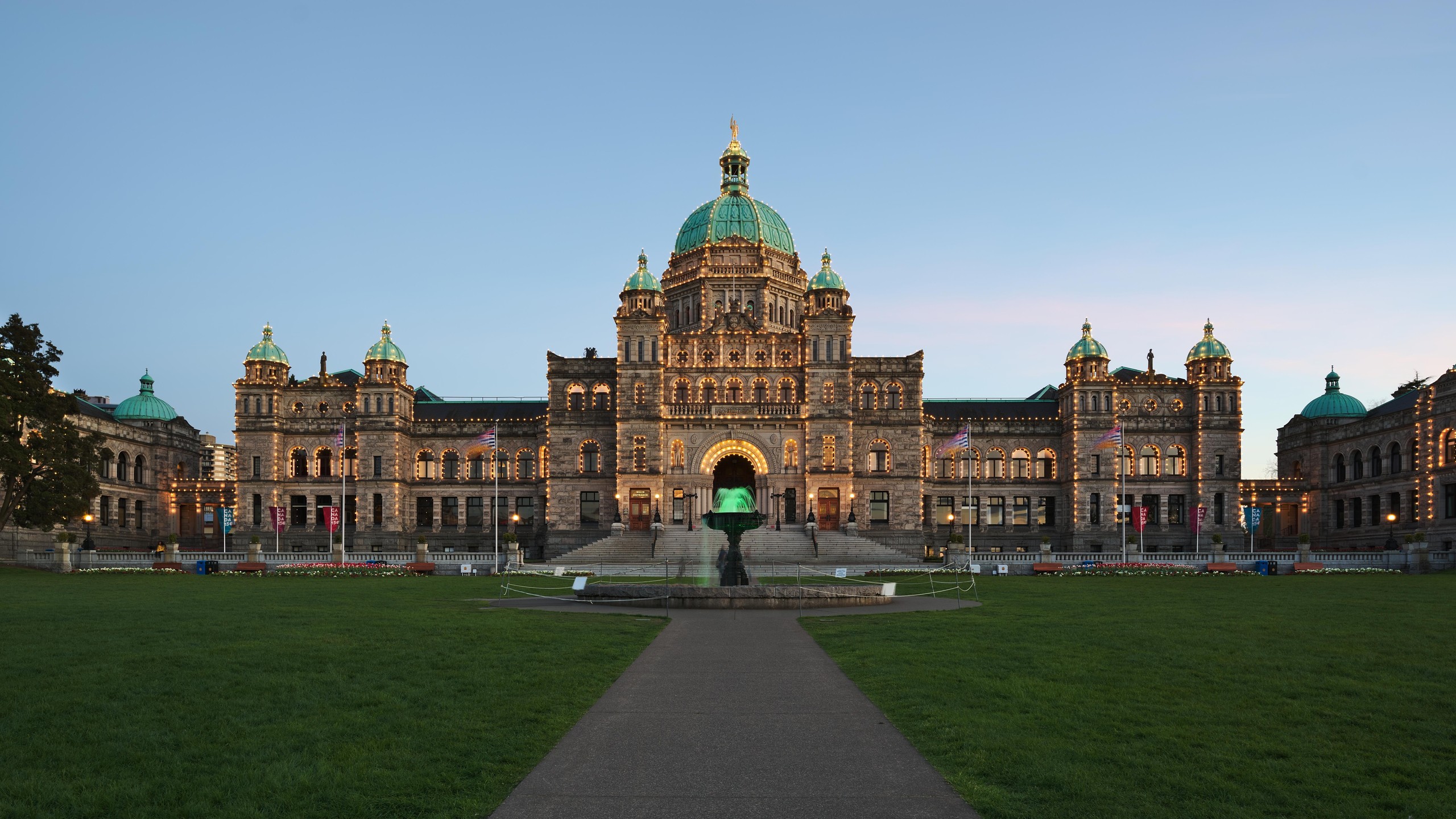 The British Columbia Parliament Buildings at dusk, domes and facade outlined in thousands of lights above the front lawn and fountain.
