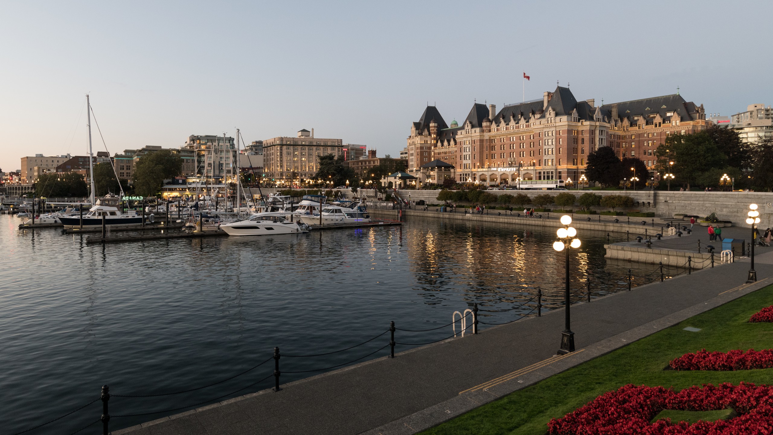 Victoria's Inner Harbour at dusk — causeway lamps lit, boats moored, the Empress Hotel above the sea wall.